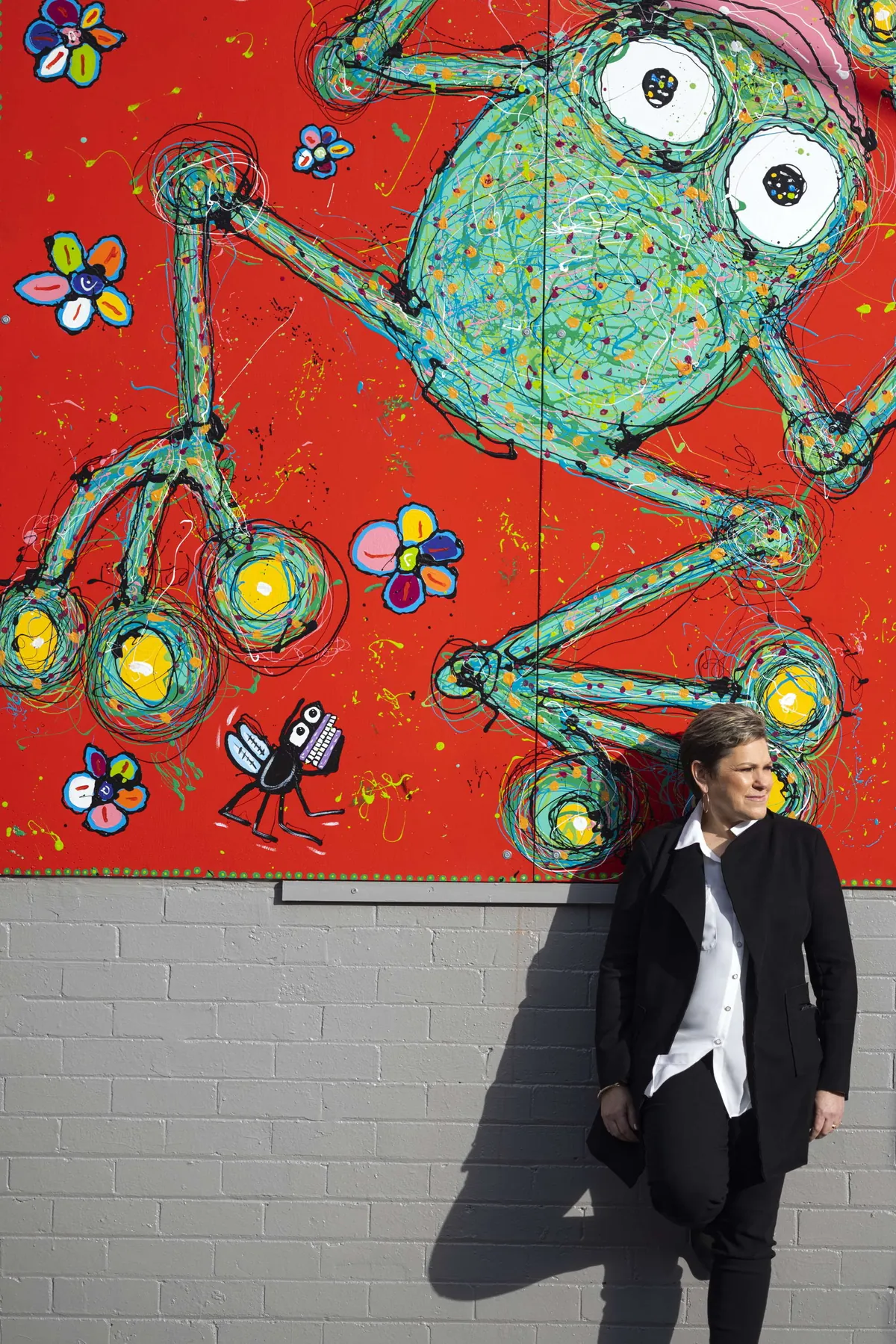 Sue leaning on a wall under a huge, bright mural of a frog