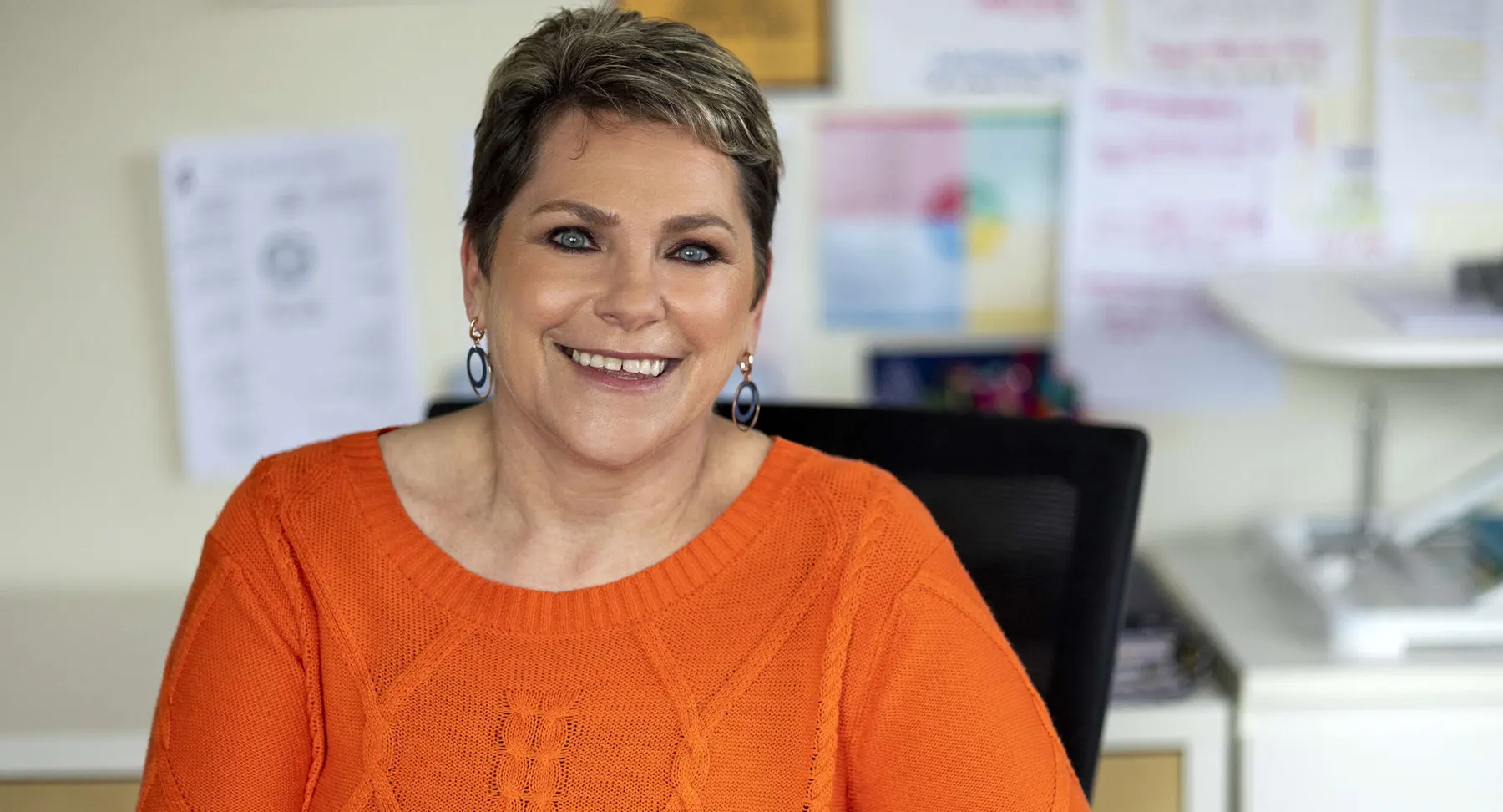 Sue smiling at her desk in her orange jumper
